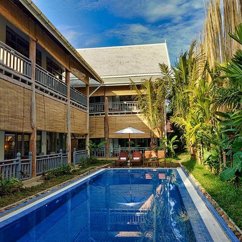 Ein einladender Pool umgeben von tropischen Pflanzen und einem stilvollen Resort mit Holzverkleidung und Sonnenschirmen.