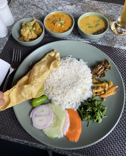 Ein Teller mit duftendem Reis, frischem Gemüse und verschiedenen würzigen Currys, serviert in einer eleganten Umgebung.