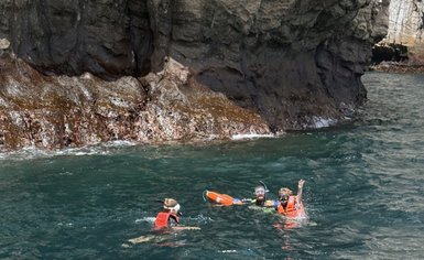 Drei Schnorchler im Wasser, umgeben von Felsen, genießen die Erkundung der Unterwasserwelt mit Schwimmwesten.