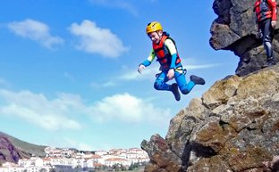 Ein Junge springt fröhlich von einem Felsen ins Wasser, während andere Teilnehmer ihn beobachten und sich vorbereiten.
