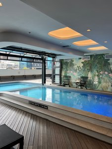 Ein eleganter Innenpool mit glattem Wasser, umgeben von einer tropischen Wandmalerei und modernen Möbeln.