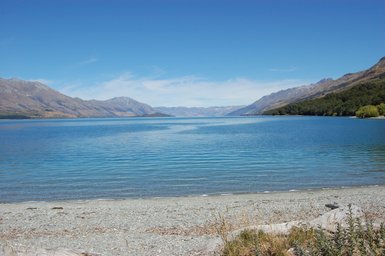 Ein ruhiger See mit klarem Wasser, umgeben von majestätischen Bergen und einem strahlend blauen Himmel.