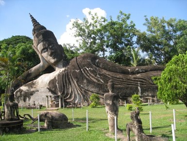 Eine massive, liegende Buddha-Statue dominiert den Park, umgeben von üppigem Grün und weiteren kleineren Statuen.