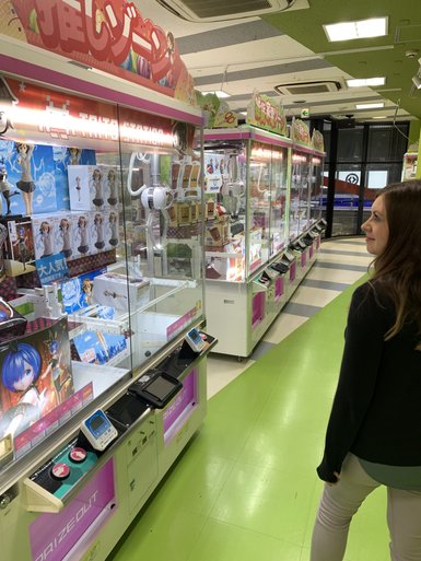 Eine Frau steht vor einer Reihe von Spielautomaten in einem hellen, bunten Raum voller Spielzeugpreise.