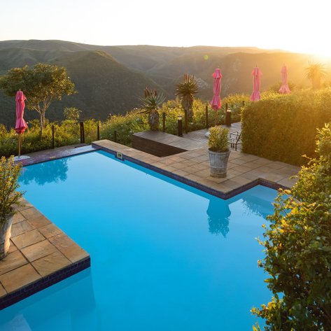 Ein glitzernder Pool spiegelt die sanften Hügel der Umgebung wider, während die Sonne am Horizont aufgeht.