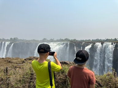 Zwei Kinder stehen am Rand eines Wasserfalls und bewundern die beeindruckende Aussicht auf die Victoriafälle.