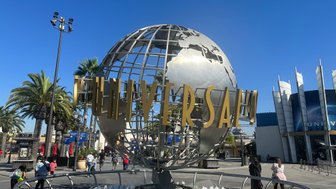 Die goldene Universal-Kugel steht im Vordergrund, umgeben von Palmen und Besuchern, die den Freizeitpark betreten.