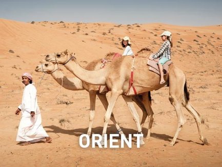 Zwei Kamele tragen Kinder durch die Wüste, während ein Mann in traditioneller Kleidung sie führt.