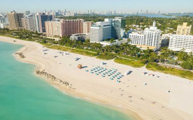 Ein atemberaubender Blick auf den Strand von Miami Beach, umgeben von modernen Hotels und Palmen unter klarem Himmel.