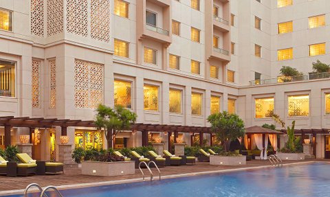 Ein eleganter Hotelpool mit Liegen und Palmen, umgeben von einem modernen Gebäude mit kunstvollen Fenstern.