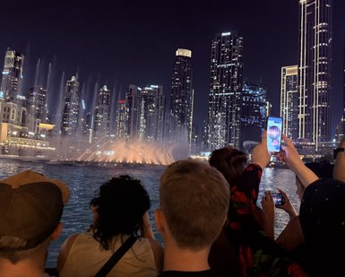 Eine Gruppe von Menschen beobachtet die beeindruckende Wasserfontäne in Dubai, während die Stadtlichter im Hintergrund leuchten.