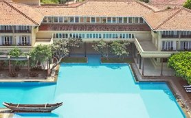 Ein weitläufiger Pool umgeben von tropischen Pflanzen und einem eleganten Gebäude mit traditioneller Architektur.