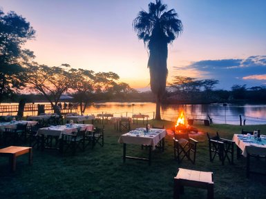 Ein malerischer Sonnenuntergang über einem See, umgeben von Tischen und Stühlen, die für ein Abendessen im Freien vorbereitet sind.