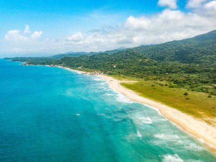Ein atemberaubender Blick auf den Strand von Tayrona, umgeben von üppigem Grün und klarem, blauem Wasser.