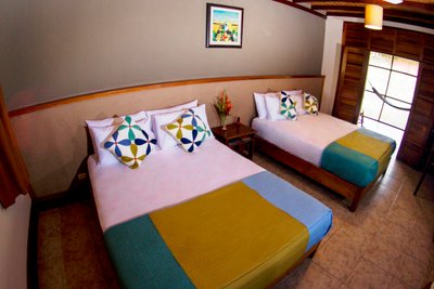 Zwei Einzelbetten mit bunten Kissen in einem hellen, einladenden Zimmer, das eine entspannte Atmosphäre ausstrahlt.