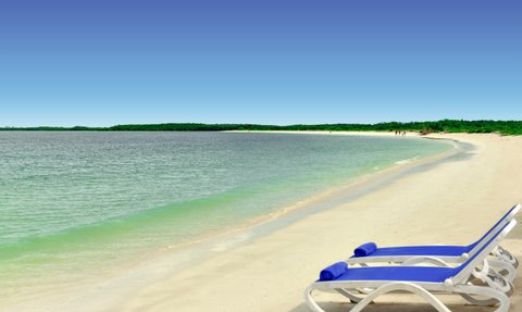 Ein ruhiger Strand mit sanften Wellen, weißen Sand und blauen Liegen, die zum Entspannen einladen.