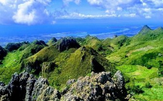 Eine atemberaubende Aussicht auf die grünen Hügel und das blaue Meer von Osmena Peak unter einem klaren Himmel.