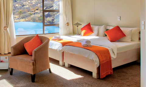 Ein helles Zimmer mit großen Fenstern, das eine atemberaubende Aussicht auf die Natur bietet, mit orangefarbenen Akzenten.