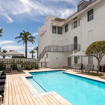 Ein einladender Poolbereich im Winchester Hotel, umgeben von Palmen und eleganten Liegen mit schwarz-weißen Streifen.