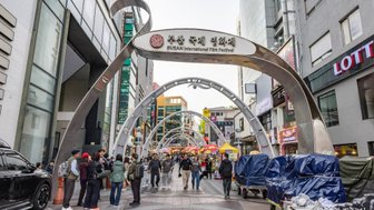 Eine belebte Straße während des Busan International Film Festivals, mit Menschen, die sich unter den geschwungenen Bögen bewegen.
