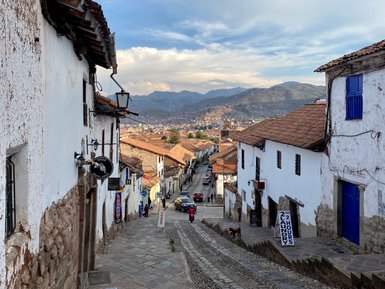 Eine steile, gepflasterte Straße in Cusco, Peru, mit weißen Häusern und blauen Fensterläden, die in die Ferne führt.
