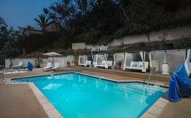 Ein einladender Poolbereich mit bequemen Liegen und Sonnenschirmen, umgeben von üppigem Grün und einem klaren Himmel.