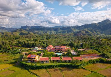 Eine malerische Ansicht des Ranomafana Hotels, umgeben von üppigen grünen Hügeln und Reisfeldern unter einem blauen Himmel.