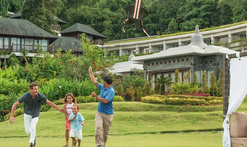 Eine Familie spielt fröhlich im Garten eines Hotels, umgeben von üppigem Grün und bunten Blumenbeeten.