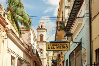 Eine belebte Straße in Havanna mit dem berühmten Restaurant 'La Bodeguita del Medio' und einer historischen Kirchturm im Hintergrund.