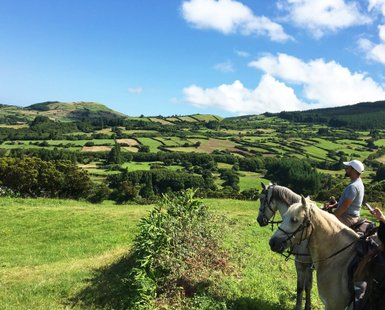Zwei Reiter auf Pferden genießen die atemberaubende Aussicht auf die grüne Landschaft unter einem strahlend blauen Himmel.