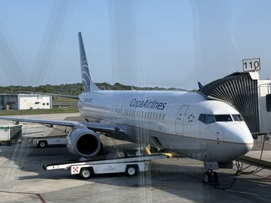 Ein Copa Airlines Flugzeug parkt am Gate 110, während Gepäck über einen Karren ausgeladen wird.