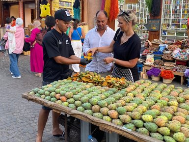 Ein Verkäufer bietet frische Früchte an einer Marktstand in Marrakesch an, umgeben von interessierten Käufern.