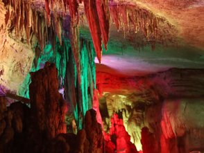Die farbenfrohe Beleuchtung hebt die beeindruckenden Stalaktiten und Stalagmiten in der Höhle hervor.
