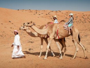 Beduine führt zwei Kamele mit zwei Mädchen durch die Wüste – Oman Familienreise