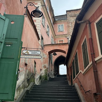 Eine enge Treppe führt durch einen historischen Durchgang, umgeben von pastellfarbenen Gebäuden und einer grauen Himmel.