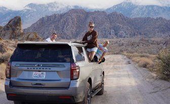 Eine Familie genießt einen Roadtrip in der Wüste, während sie fröhlich aus einem SUV herausblickt.
