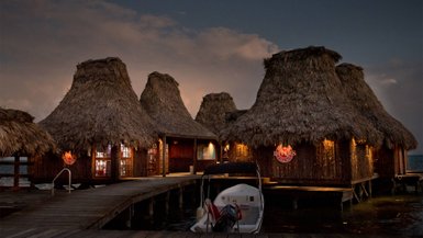 Die strohgedeckten Hütten des Resorts strahlen in der Dämmerung, während ein Boot am Steg festgemacht ist.