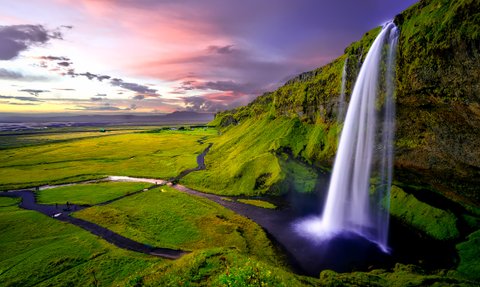 Ein majestätischer Wasserfall stürzt über grüne Klippen, während der Himmel in sanften Pastellfarben leuchtet.