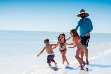 Ein Vater spielt mit seinen Kindern am Strand, während sie fröhlich im Wasser planschen und lachen.