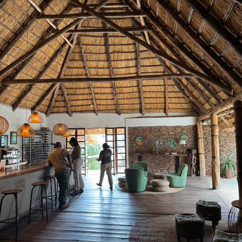 Ein einladender Empfangsbereich mit einem hohen Strohdach, warmen Lichtquellen und stilvollen Möbeln aus Naturmaterialien.
