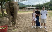 Ein Elefant steht in einem Gehege, während eine Frau und zwei Kinder lächeln und sich ihm nähern.