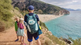 Eine Familie wandert auf einem Pfad mit Blick auf einen schönen Strand und das klare, blaue Wasser des Meeres.