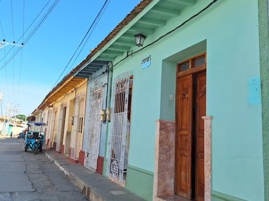 Bunte Häuser mit verschiedenen Fassaden stehen an einer ruhigen Straße unter einem strahlend blauen Himmel.