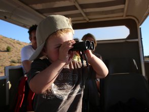 Ein kleiner Junge mit einer Baseballmütze schaut durch ein Fernglas, während er in einem Fahrzeug sitzt und die Landschaft erkundet.
