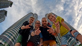 Familie posiert fröhlich für ein Selfie mit den Petronas Twin Towers im Hintergrund – Malaysia & Borneo Reise mit Kindern
