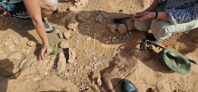 Zwei Personen untersuchen den Boden in einer felsigen Umgebung, während sie nach Dinosaurierfossilien suchen.