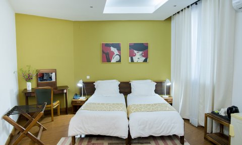 Ein modernes Hotelzimmer mit zwei Einzelbetten, stilvollen Bildern an der Wand und einem Schreibtisch in warmen Farben.