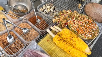 Ein Straßenstand in Vietnam bietet eine Vielzahl von köstlichen Speisen, darunter gegrillte Würstchen und frisches Gemüse.