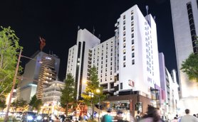 Ein modernes Hotelgebäude mit beleuchteten Fenstern, umgeben von urbaner Architektur und nächtlicher Atmosphäre.
