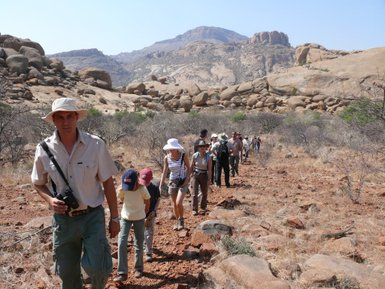 Eine Reisegruppe wandert gemeinsam auf einem schmalen Pfad durch die Natur - Namibia mit Kindern